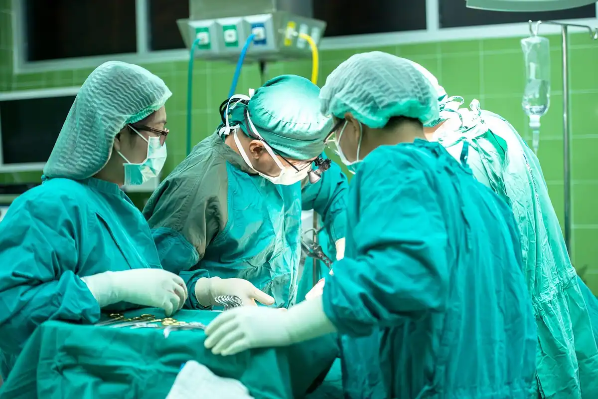 Echipă de chirurgi în costume verzi care operează un pacient în sala de operații