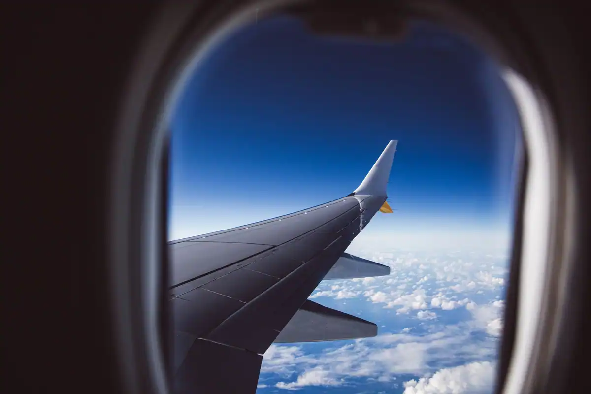 Aripa avionului și norii văzuți prin hublou în timpul unui zbor de zi