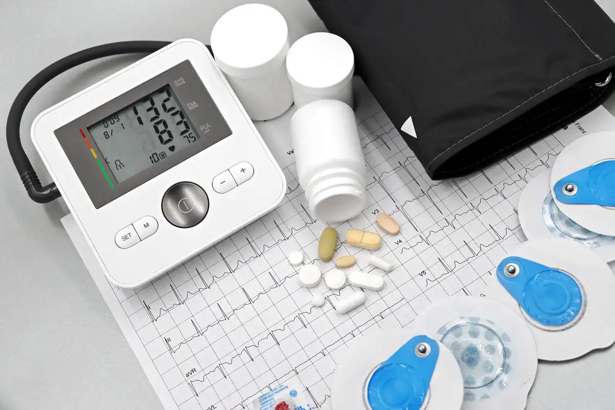 Tensiometru, pastile și o electrocardiogramă așezate pe o suprafață plană