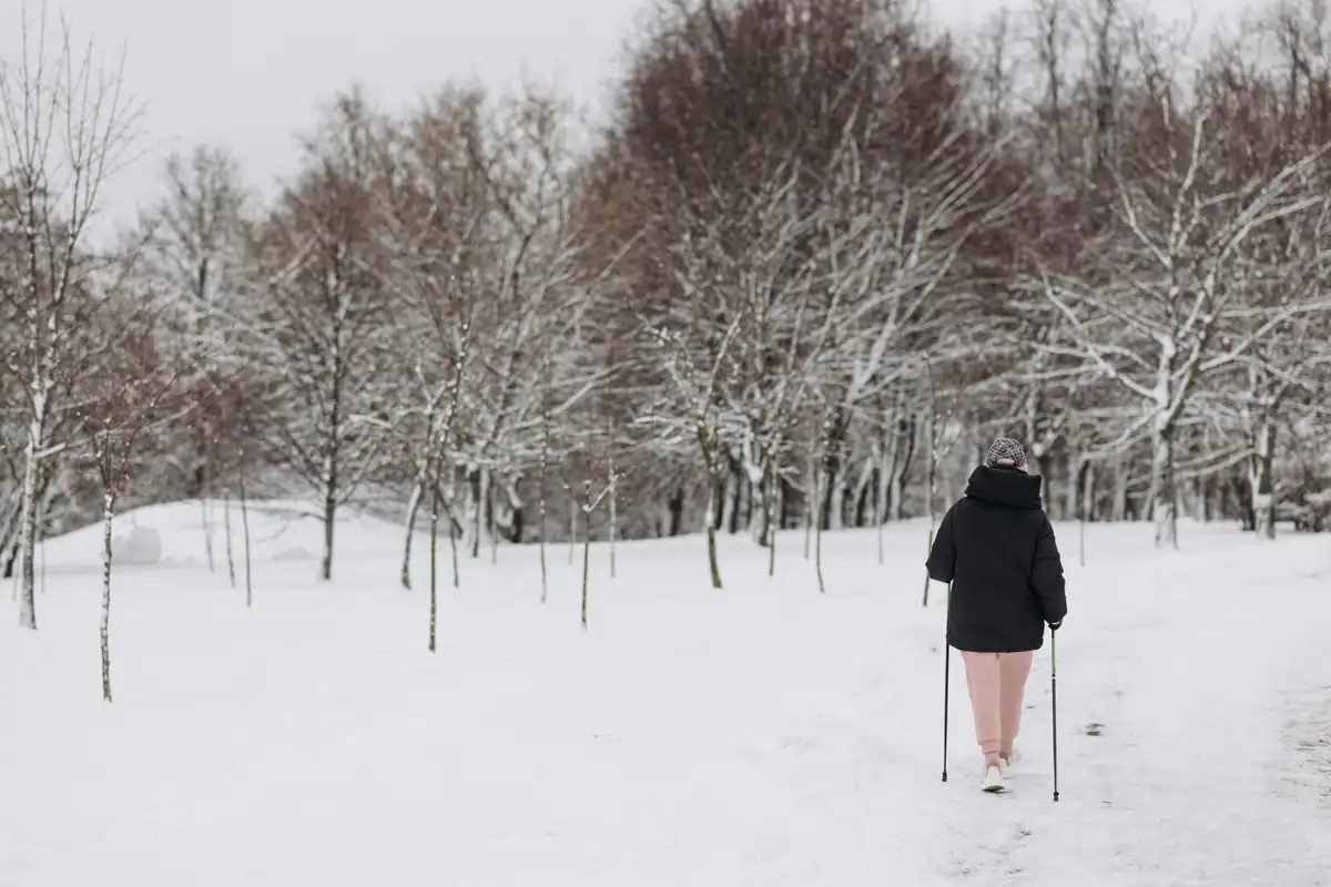 Femeie care se plimbă într-un parc acoperit de zăpadă, într-o zi rece de iarnă