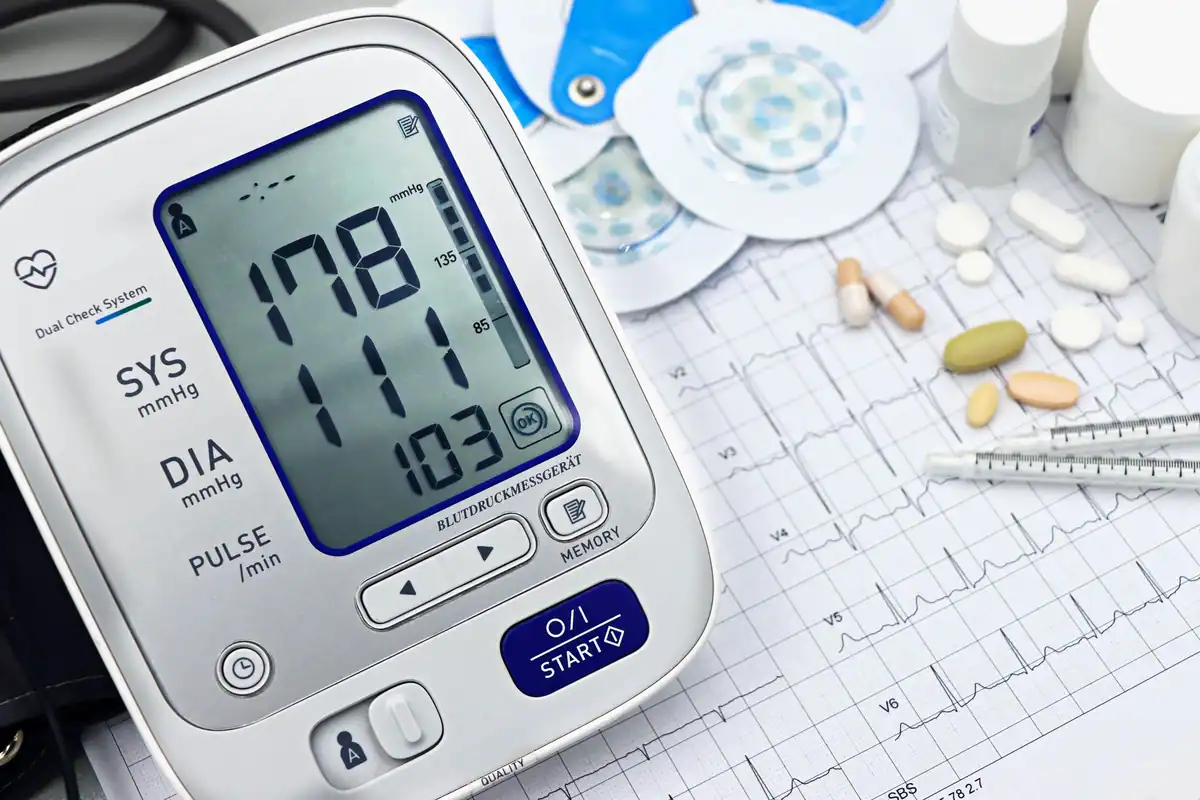 Tensiometru digital lângă un traseu EKG, pastile și instrumente medicale