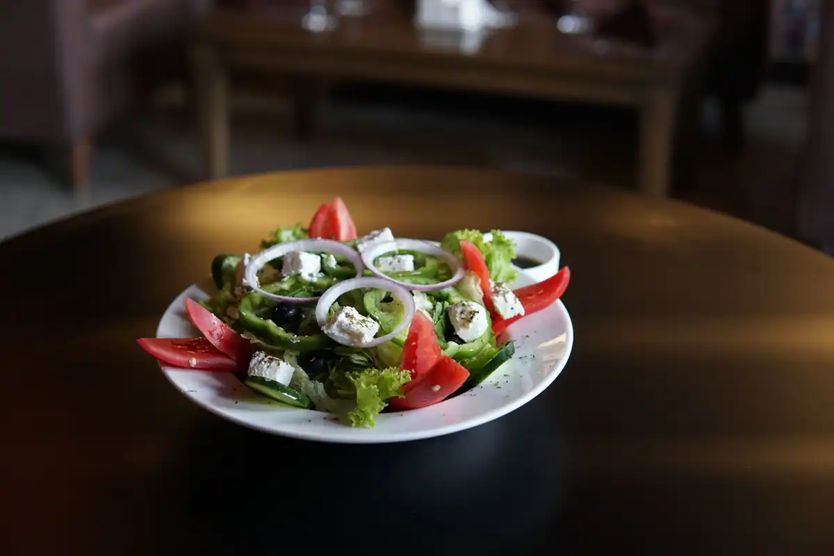 Salată grecească cu brânză feta, roșii, măsline și verdețuri pe o masă rotundă