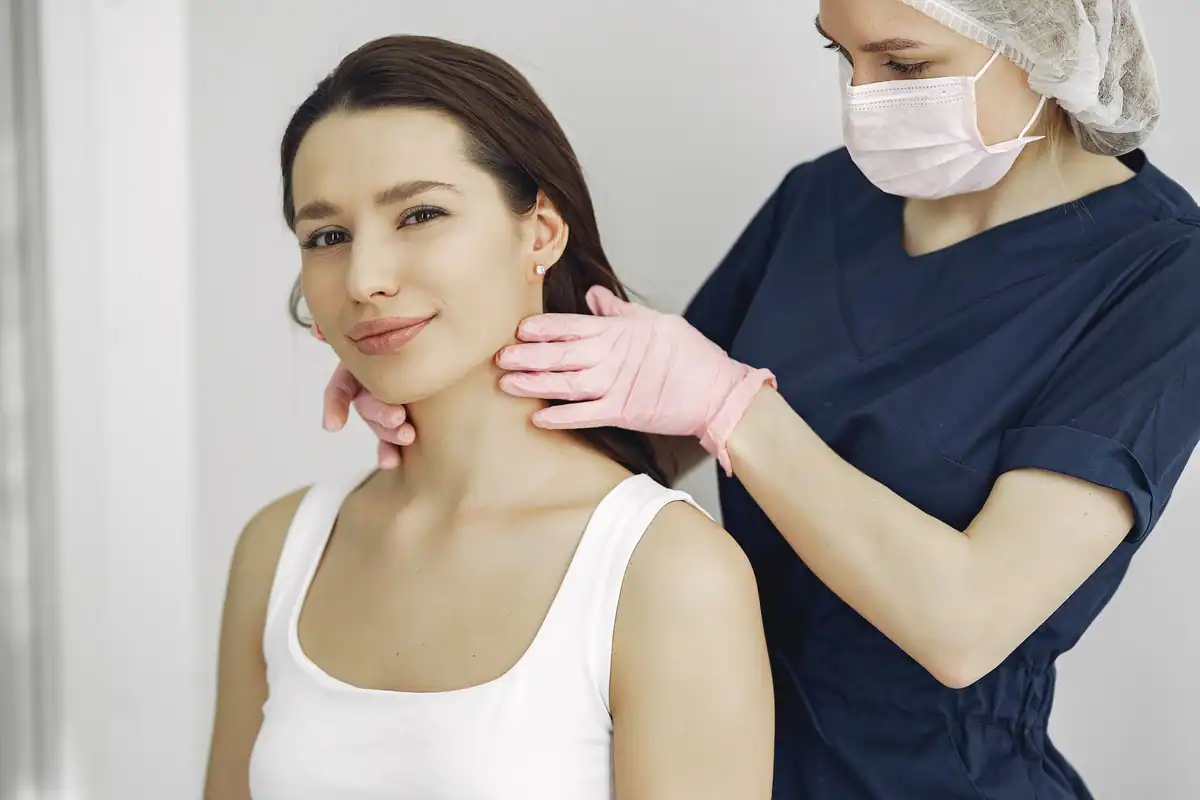 Cadru medical în costum de spital care examinează gâtul unei femei zâmbitoare