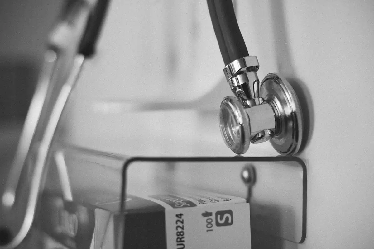 Stetoscop atârnat pe un suport metalic într-un cabinet medical, fotografie alb-negru
