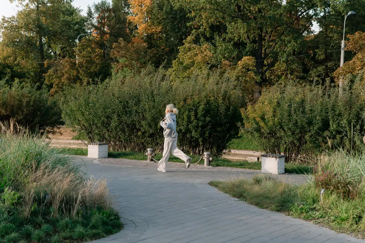 Femeie vârstnică ce aleargă activ printr-un parc plin de verdeață