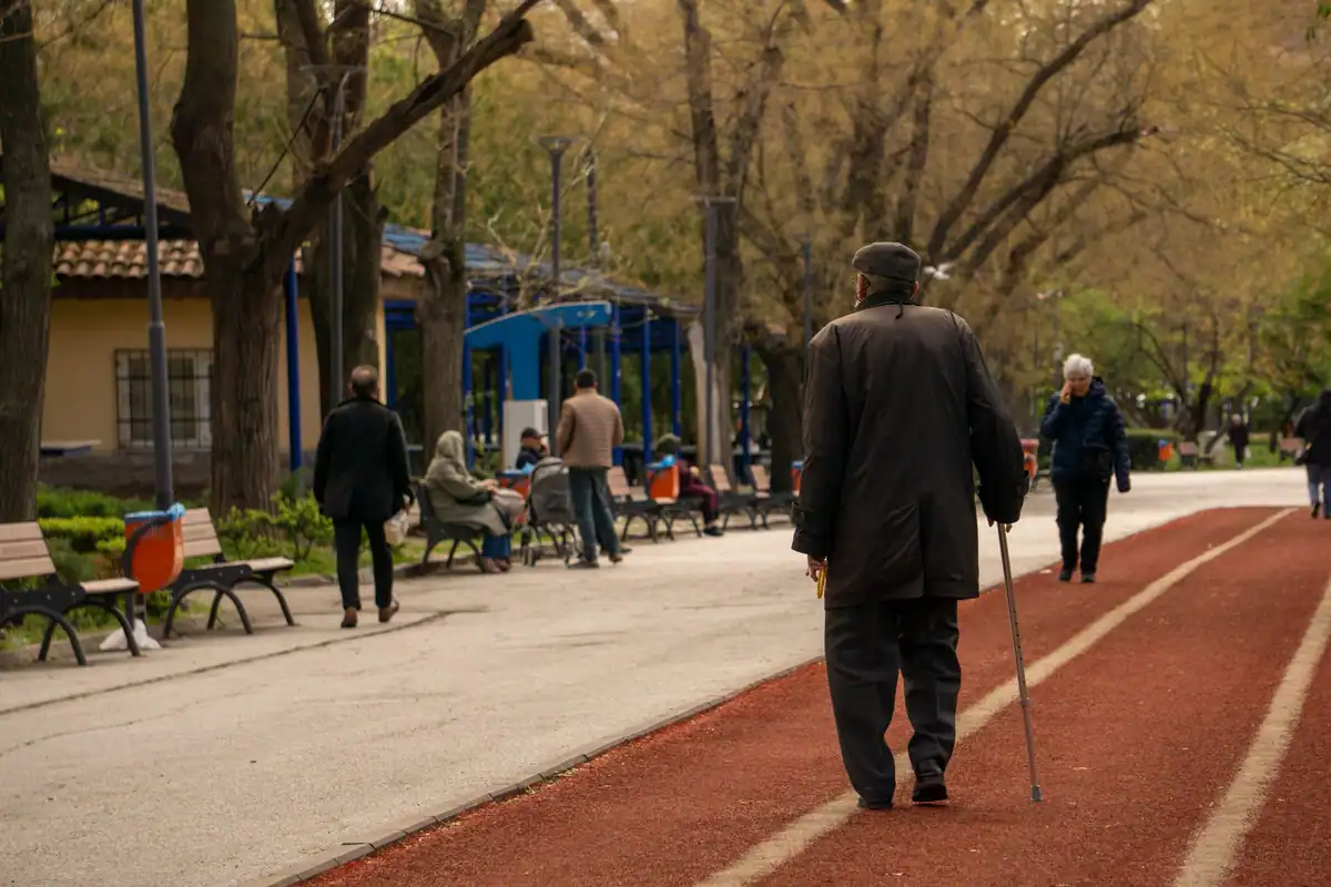 Bărbat vârstnic cu baston care se plimbă pe o alee din parc