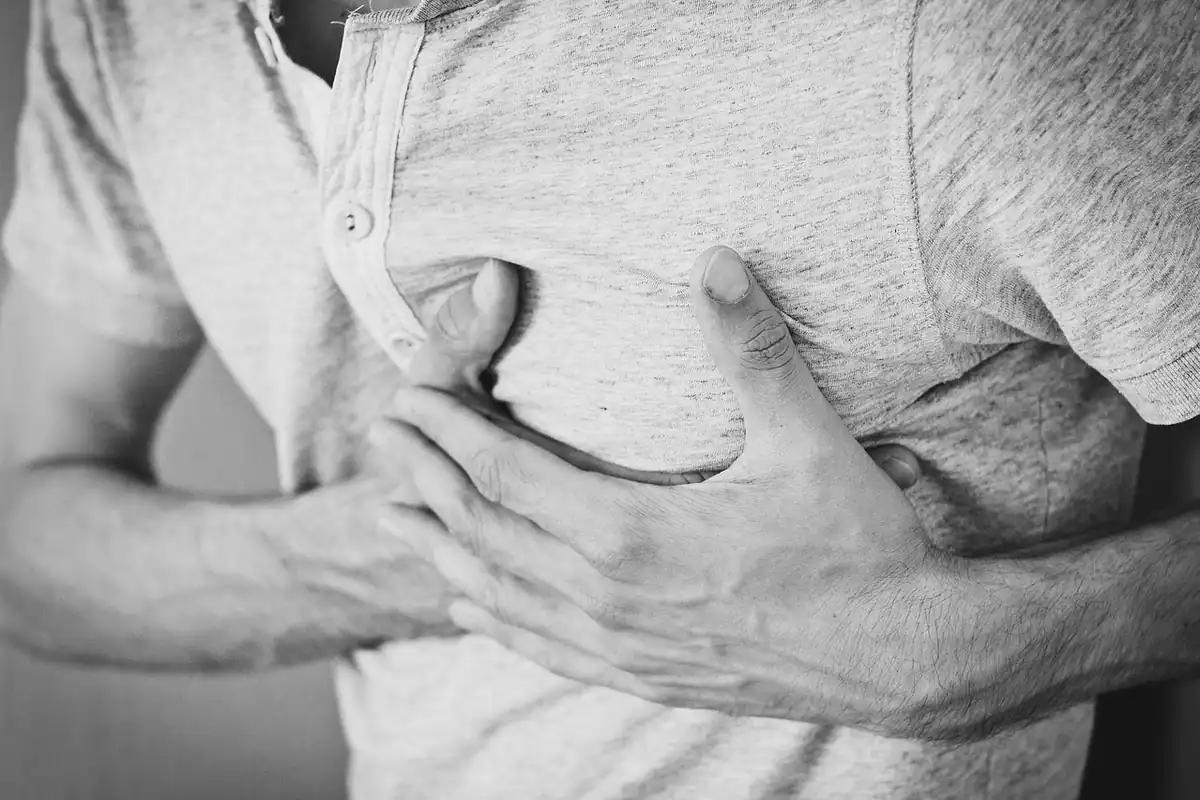 Bărbat care își ține ambele mâini pe piept, simțind bătăi neregulate ale inimii