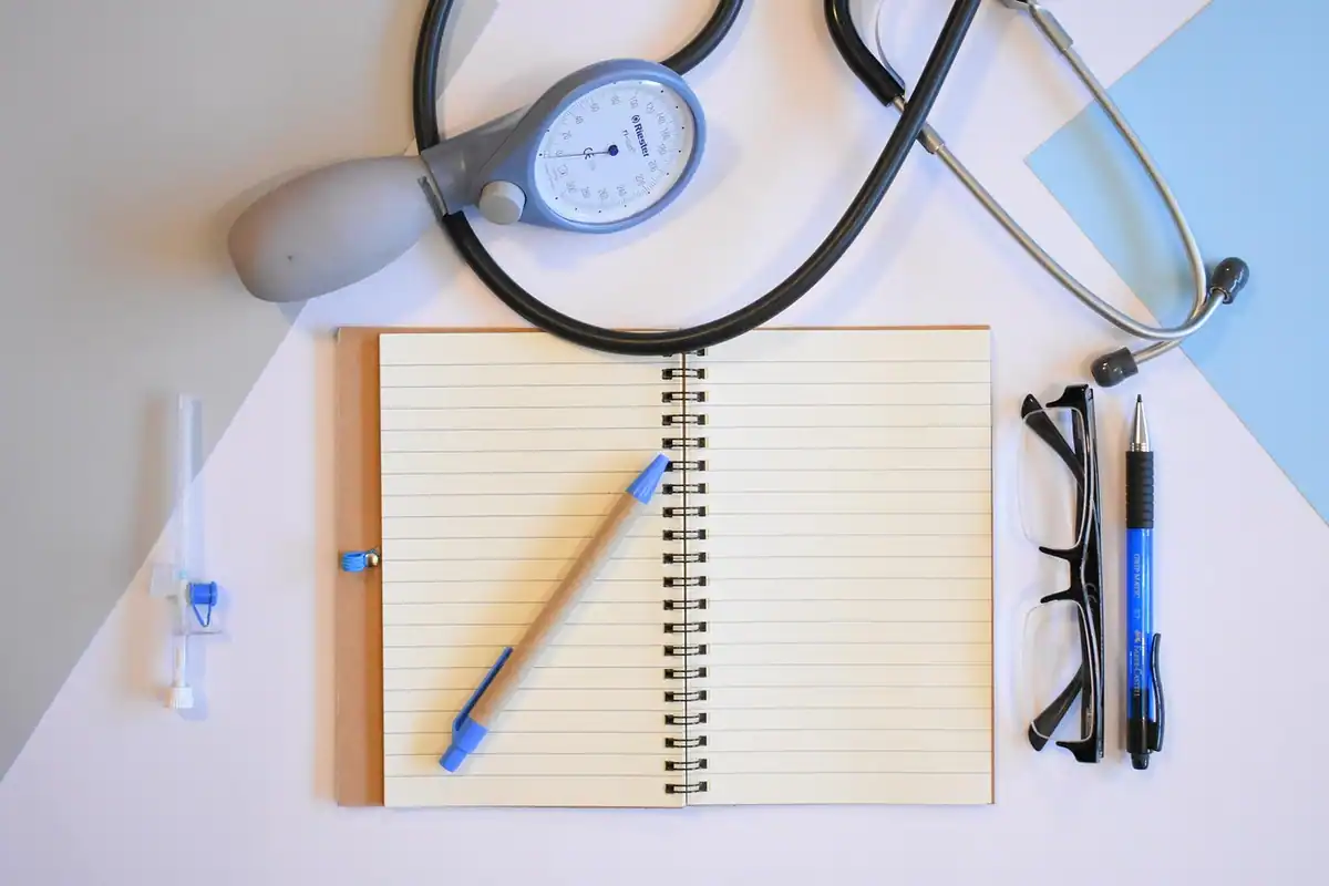 Medic care scrie notițe în timpul unei consultații, cu cafea și laptop pe masă, văzut de sus
