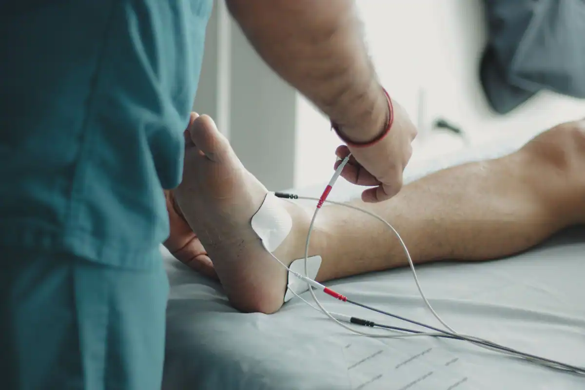 Cadru medical care examinează piciorul unui pacient cu aparatură în spital